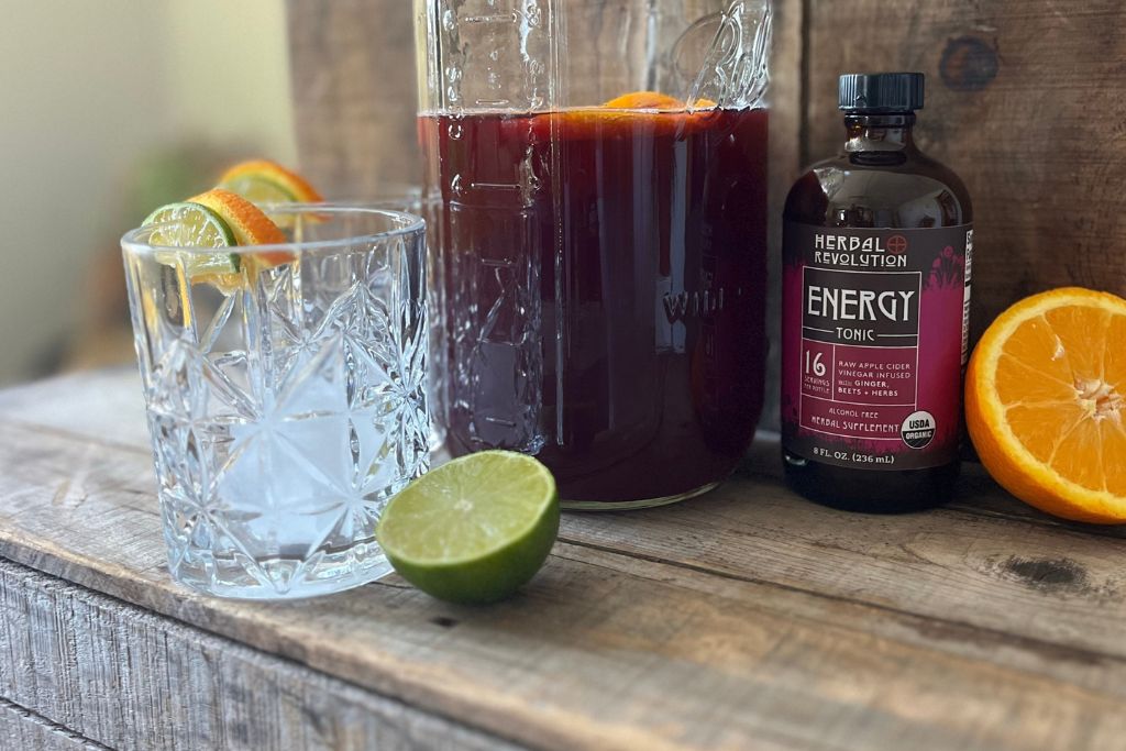 Glass jar of Energy Tonic Sangria with citrus fruits and bottle of Herbal Revolution Energy Tonic
