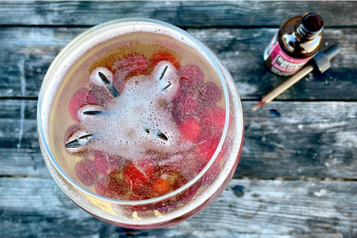 Two bulb wine glasses in the background filled with an herbal drink and bright fresh cranberries and rosemary with two bottles of elderberry tonic and elixir on a wooden table with a wooden background 
